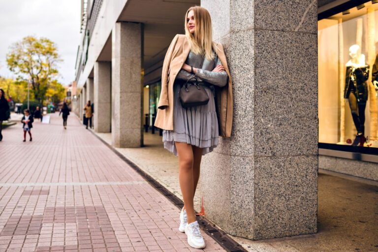 Outdoor Lifestyle Fashion Portrait Pretty Elegant Glamour Blonde Woman With Long Legs Wearing Trendy Sneakers Dress Sweater Coat Posing Europe City Traveling Alone 1 768x512